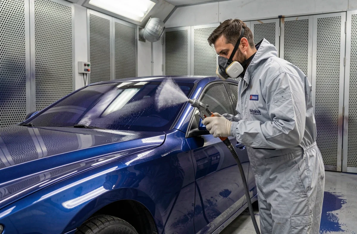 Spécialiste en finition appliquant une couche de vernis dans une cabine de peinture chez Carrosserie VLM à Montpellier