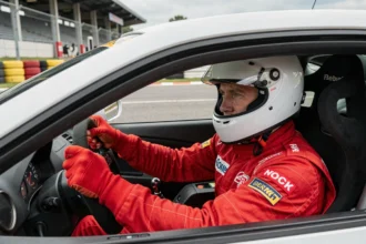 Pilote en combinaison rouge concentré dans l'habitacle d'une voiture de piste lors d'un stage de pilotage